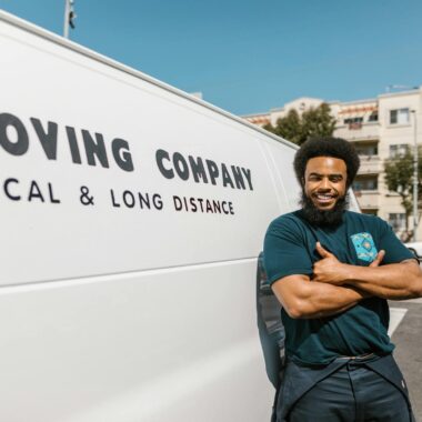 A cheerful mover standing confidently beside a moving company's van, ready for local or long distance relocation services.