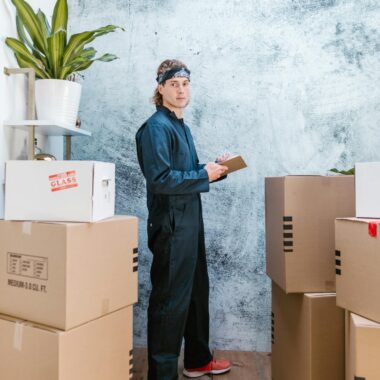 A mover in coveralls with bandana checks packages in a warehouse.