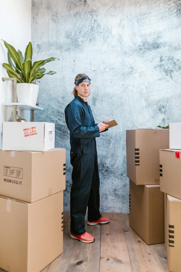 A mover in coveralls with bandana checks packages in a warehouse.