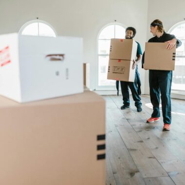 Two movers in uniform carrying boxes in a bright, new home setting.